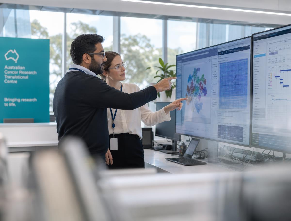 Australian researchers reviewing health data on large monitors in a modern research space